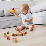 baby boy sitting on floor and playing with toys in living room
