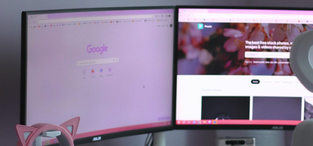Stylish home office desk setup with dual monitors, cat ear headphones, and rainbow mug.